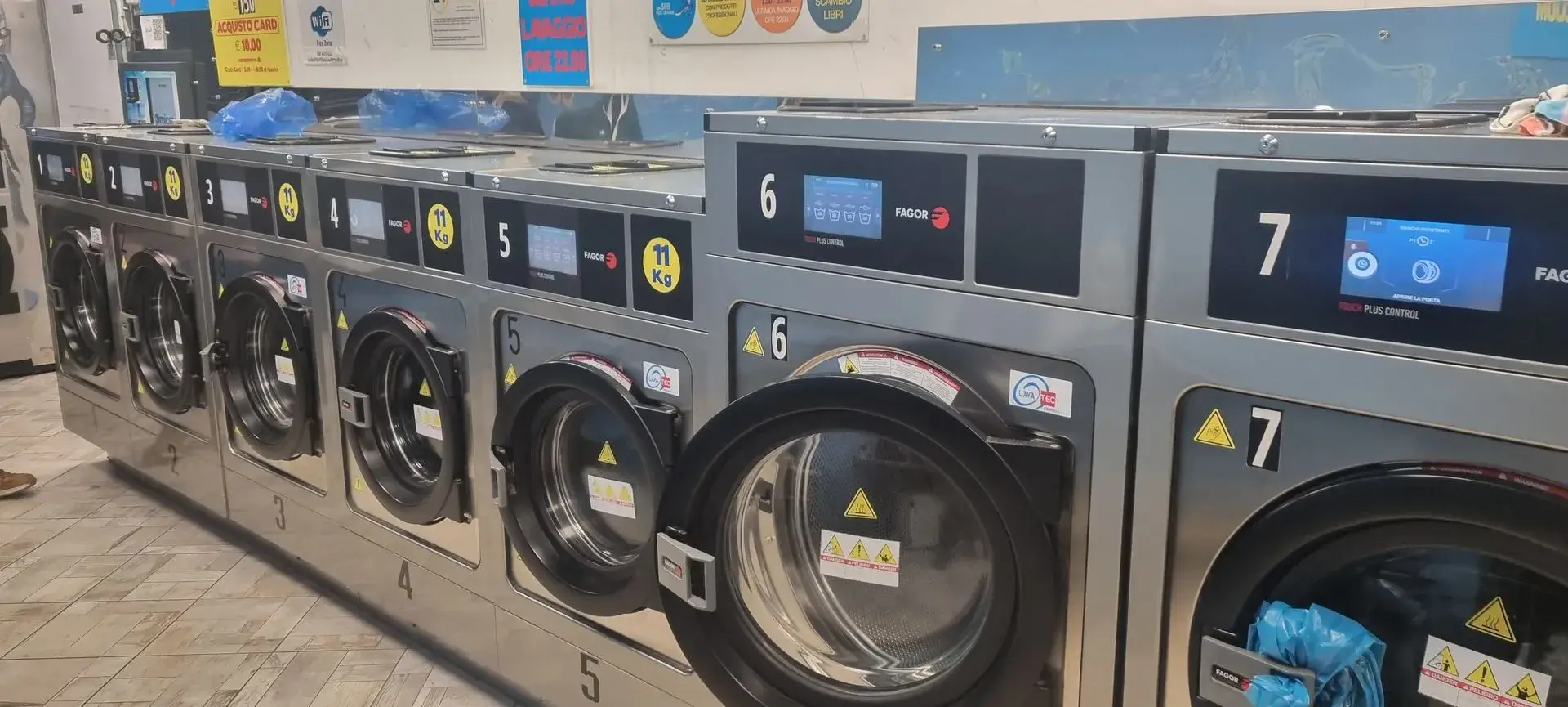 Fila di lavatrici e asciugatrici professionali Fagor nella sala della lavanderia self service